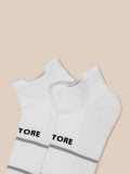 Close up of white ankle socks showing Castore branding and grey stripes on beige background