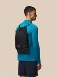Model wearing the black Castore gym sack as a backpack with drawstrings against a beige background