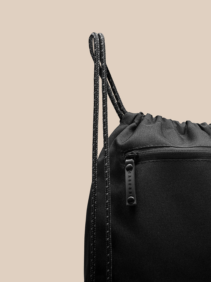 Close-up of black polyurethane gym sack showing drawstring cords and a zippered pocket with Castore branding