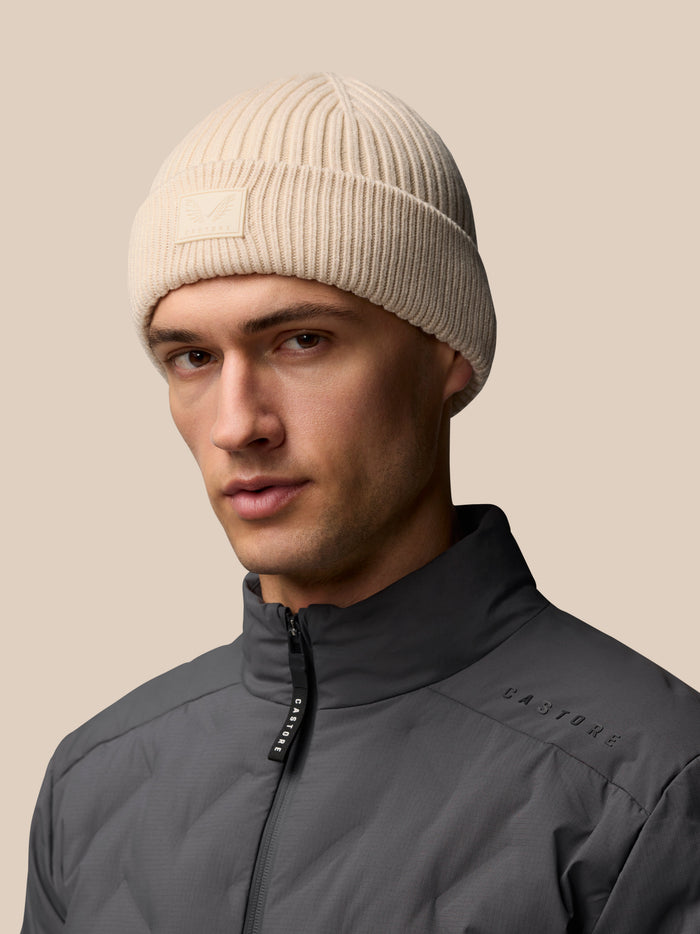 Stone colored ribbed knit beanie with Castore logo on the foldover.
