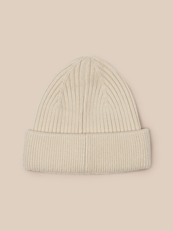 Beige ribbed knit beanie on a model with the Castore badge at the front