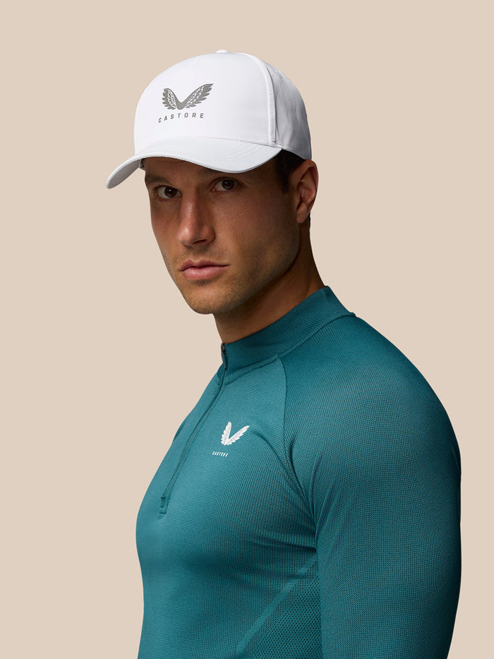 White nylon cap with halo eyelets and adjustable back strap worn by a man in a teal athletic top with Castore logo.