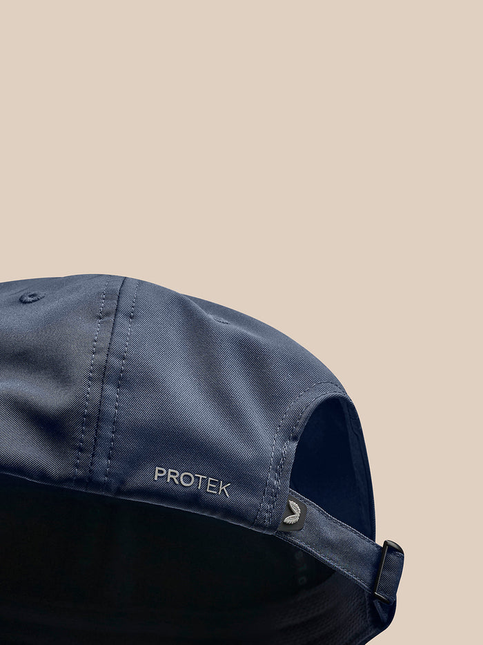 Close-up of navy cap showing PROTEK branding on the side with an adjustable back strap.