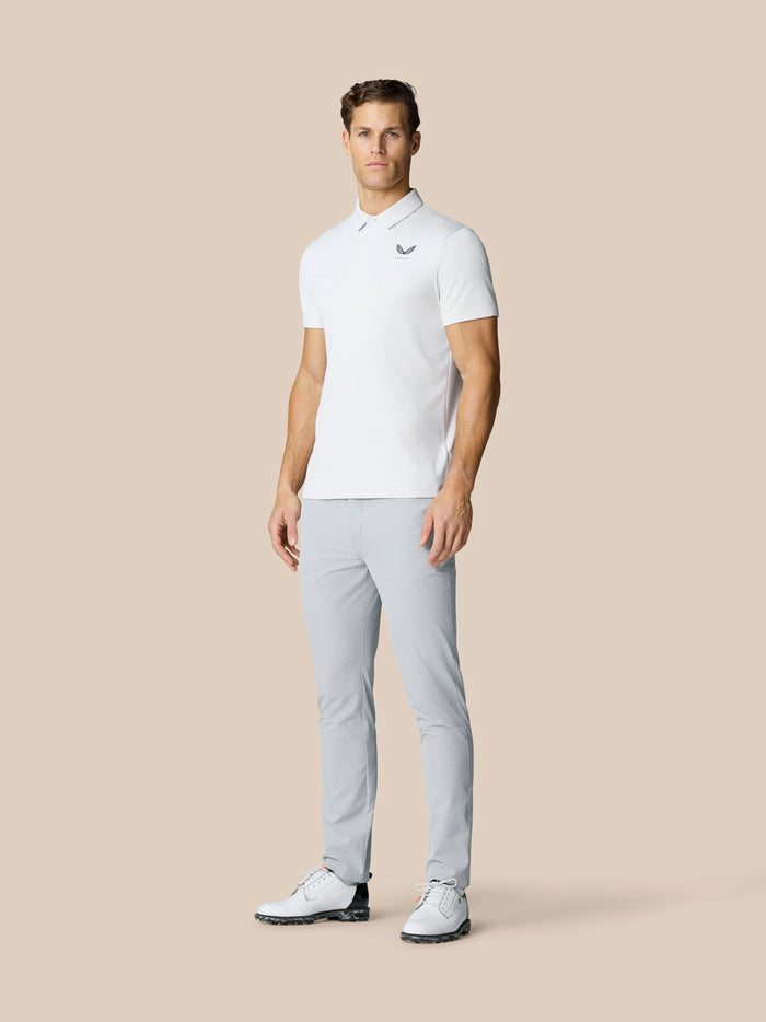 Full body shot of a man in a white polo and light grey Golf Club Trousers, showcasing modern golf attire