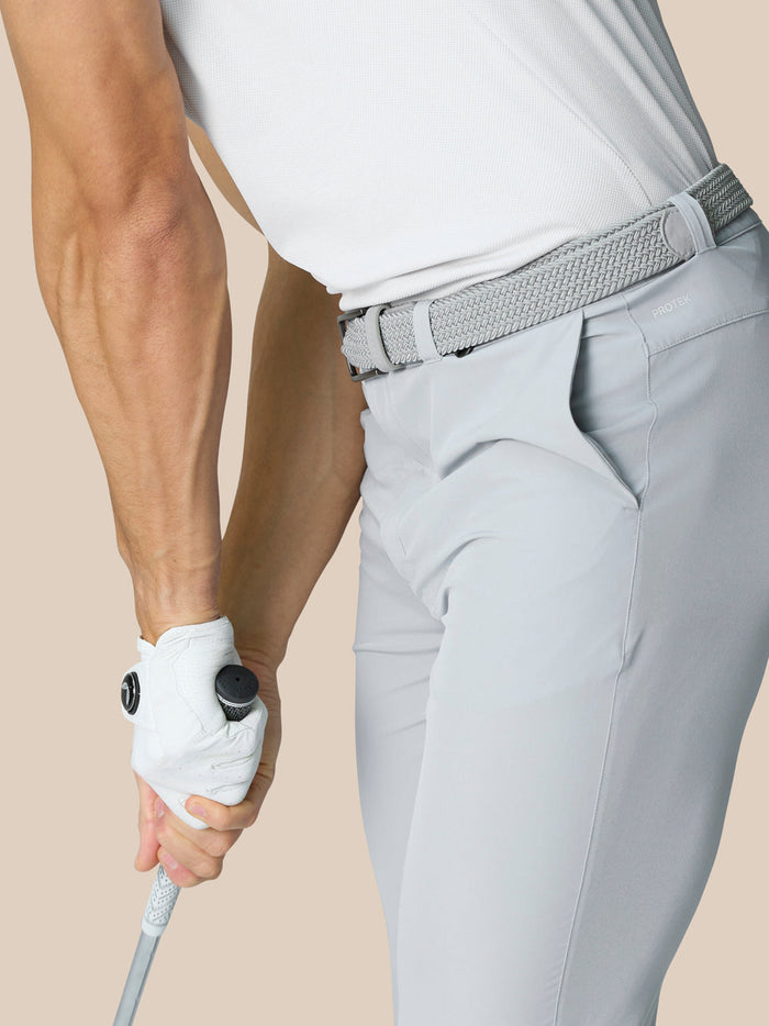 Side view of a golfer in light grey Golf Club Trousers with a woven belt holding a club.