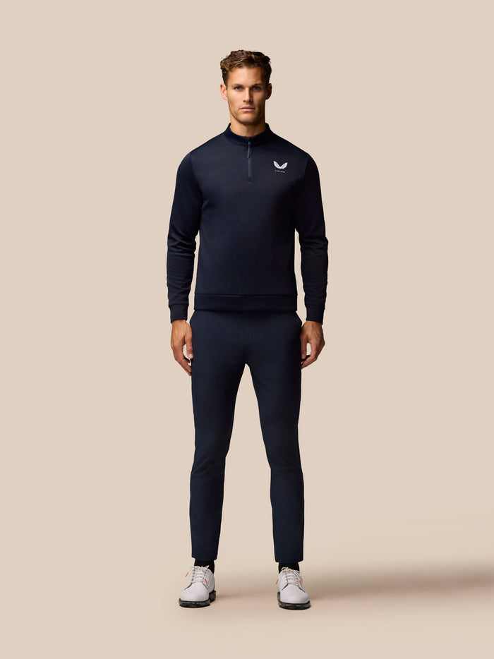 Male model wearing navy Golf Club Trousers with a matching long sleeve top on a beige backdrop