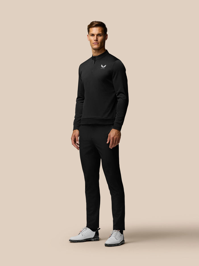 Male model wearing black golf trousers with a matching black top and white golf shoes.