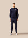 Full body front view of a man in navy Castore golf tracksuit with a chest logo and matching pants and white shoes