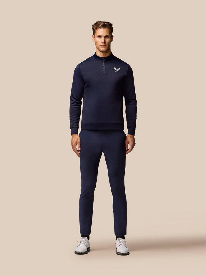 Full body front view of a man in navy Castore golf tracksuit with a chest logo and matching pants and white shoes