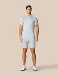 Full body shot of a man in light grey golf polo and shorts on a beige background