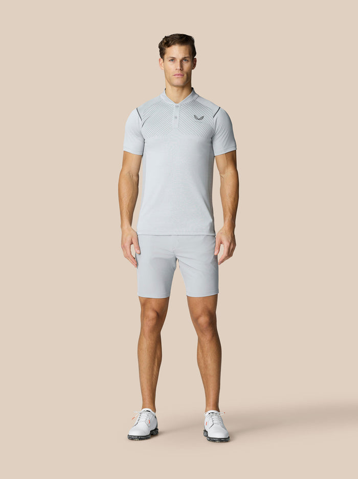 Full body shot of a man in light grey golf polo and shorts on a beige background