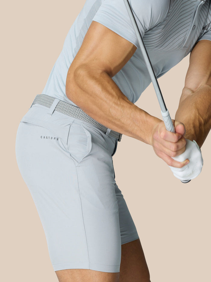 Side view of model in light grey golf shorts with a woven belt and branding on the back pocket while gripping a golf club