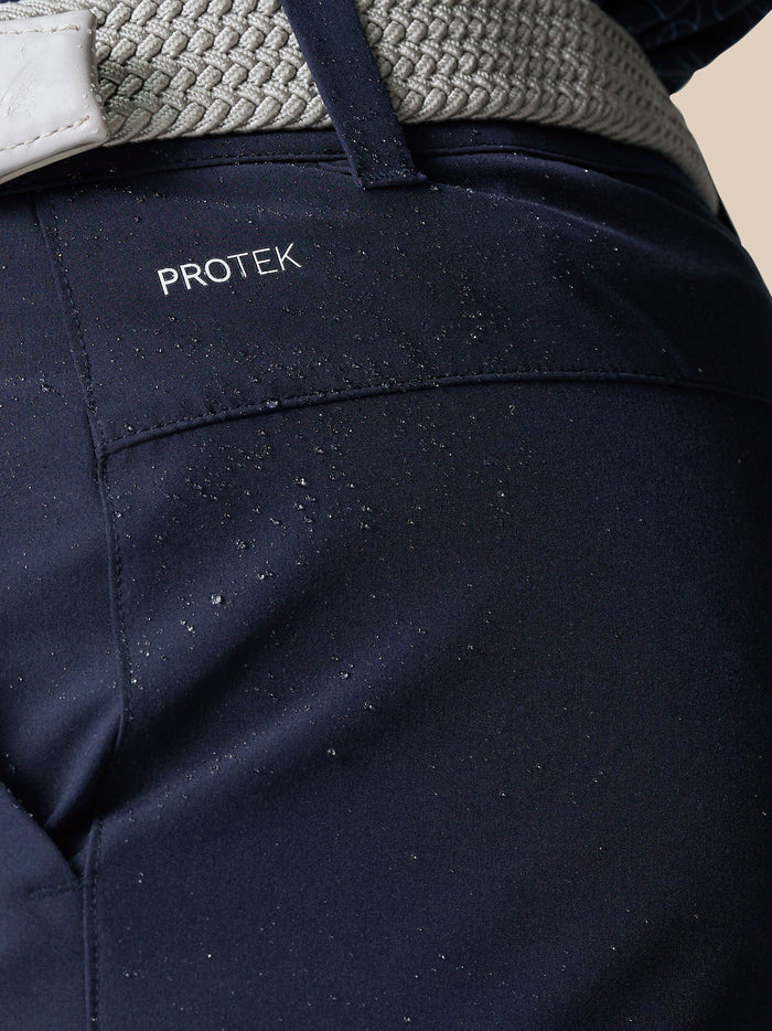 Close up of navy golf shorts with a gray woven belt showing back pocket and ProTek branding at left rear waistband.