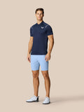 Male model wearing sky blue golf shorts with a navy polo on a beige backdrop