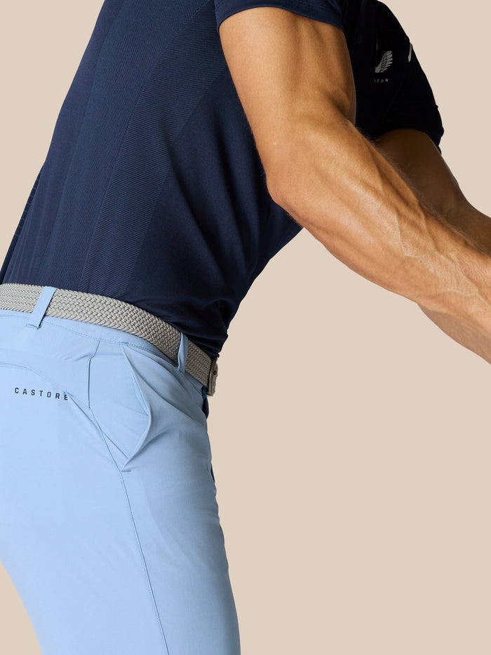 Side view of a golfer wearing a navy polo and sky blue shorts with a woven belt and Castore branding on the back pocket