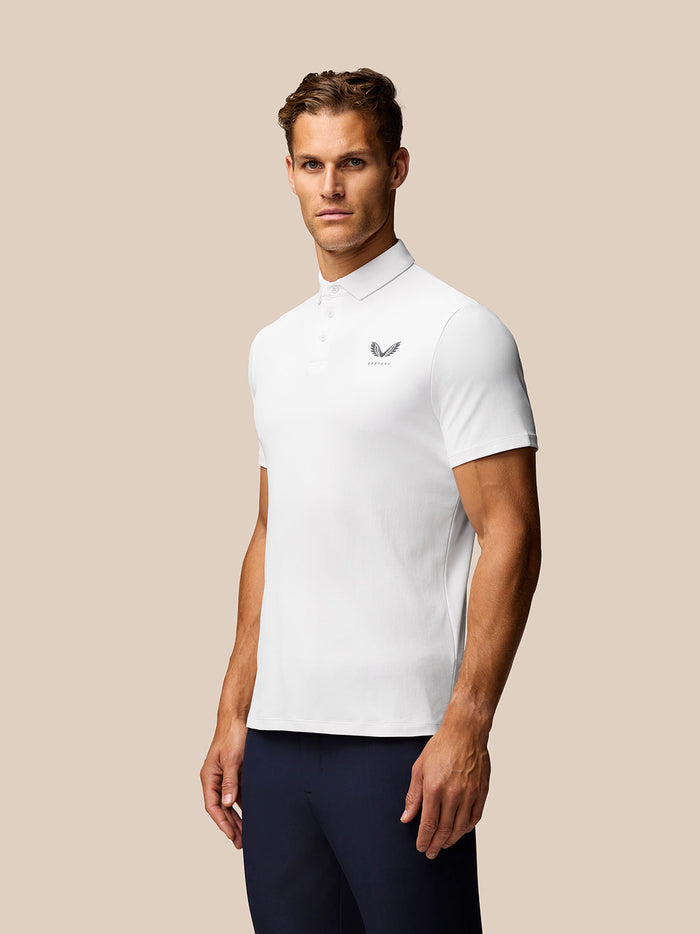 Male model wearing white Golf Club Essential Polo with Castore logo on left chest in a studio.