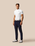 Full-length shot of a man wearing the Golf Club Essential Polo in white with navy golf pants and white shoes against a beige backdrop.