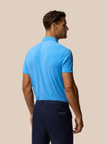 Back view of a man in a light blue Golf Club Essential Polo with a vertical Castore logo on the upper back and navy trousers.