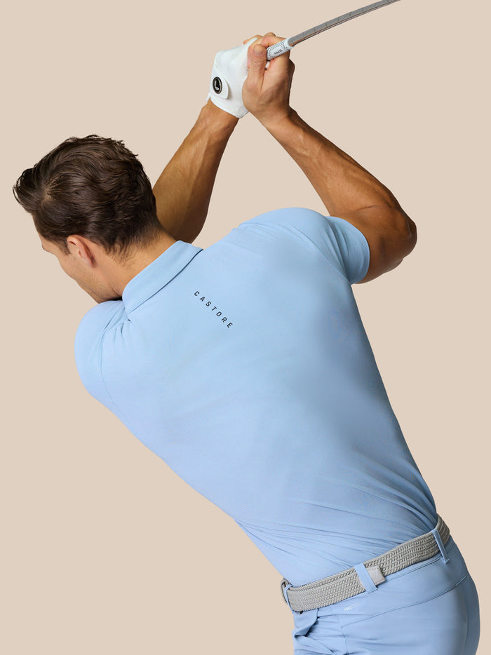 Golfer in Sky Blue Golf Club Essential Polo mid swing with Castore branding along the back and chest