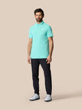 Full body shot of a man wearing the light aqua Golf Club Essential Polo with dark trousers and white golf shoes.