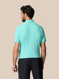 Back view of a man wearing a light aqua Castore golf polo with vertical branding on the upper back.