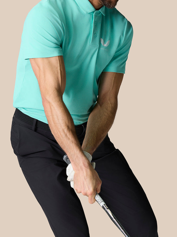 Back and side view of a man in a light aqua polo with Castore crest on the chest and vertical branding on the back.