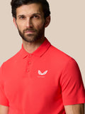 Close-up of red Golf Club Essential Polo highlighting white Castore logo on left chest.