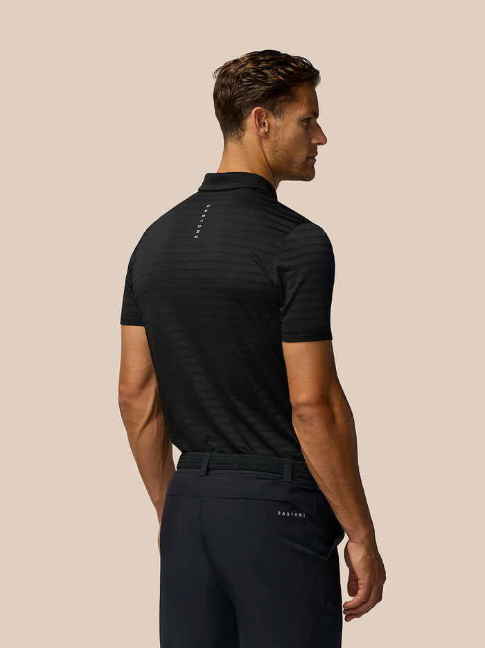 Back view of a model wearing Golf Pinnacle Pique Stripe Polo in black with all over stripes and Castore branding on the upper back