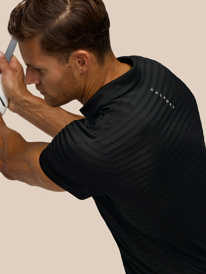 Close-up of a golfer gripping a club in the Pinnacle Polo showing striped fabric and Castore branding with Protek on the pants
