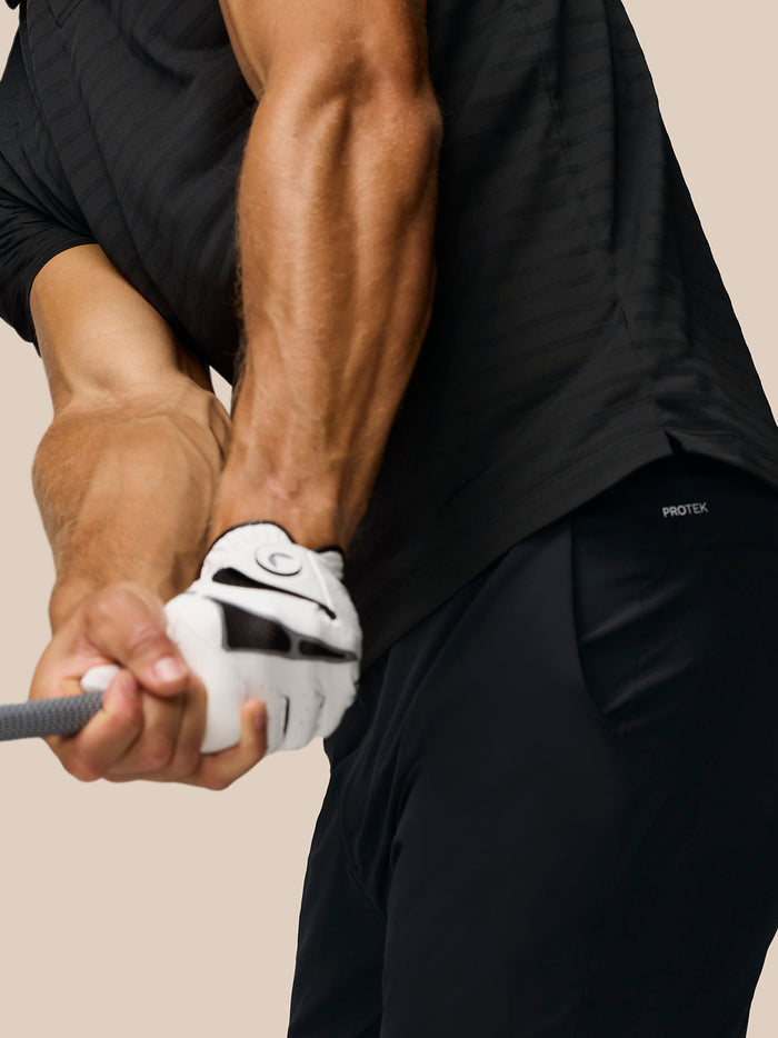 Side-back view of a man in the Golf Pinnacle Pique Stripe Polo in black alloy with stripes and Castore branding on the upper back