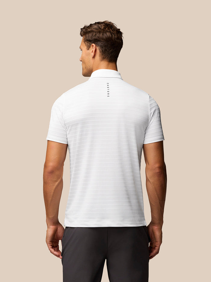 Back view of a model wearing Golf Pinnacle Pique Stripe Polo in white with stripes and Castore branding on upper back.