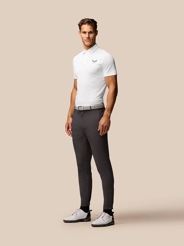 Male model in a white textured polo with stripes and gray trousers, posed in profile.
