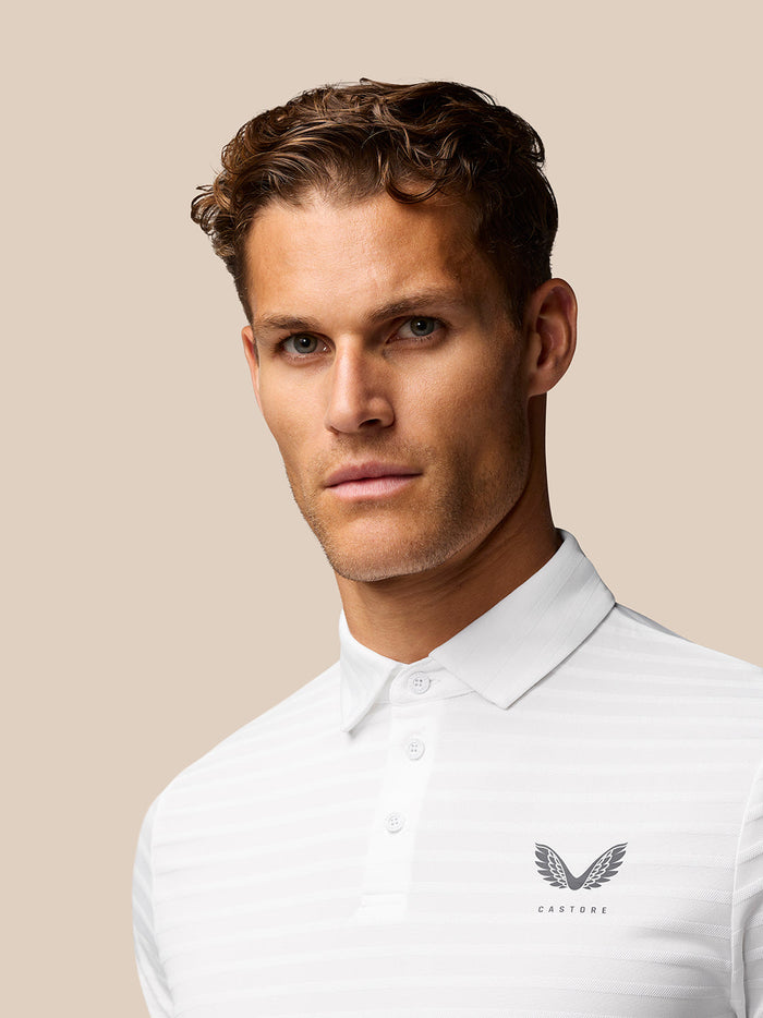 Close-up of a model in Golf Pinnacle Pique Stripe Polo highlighting the white textured fabric and left chest Castore logo.
