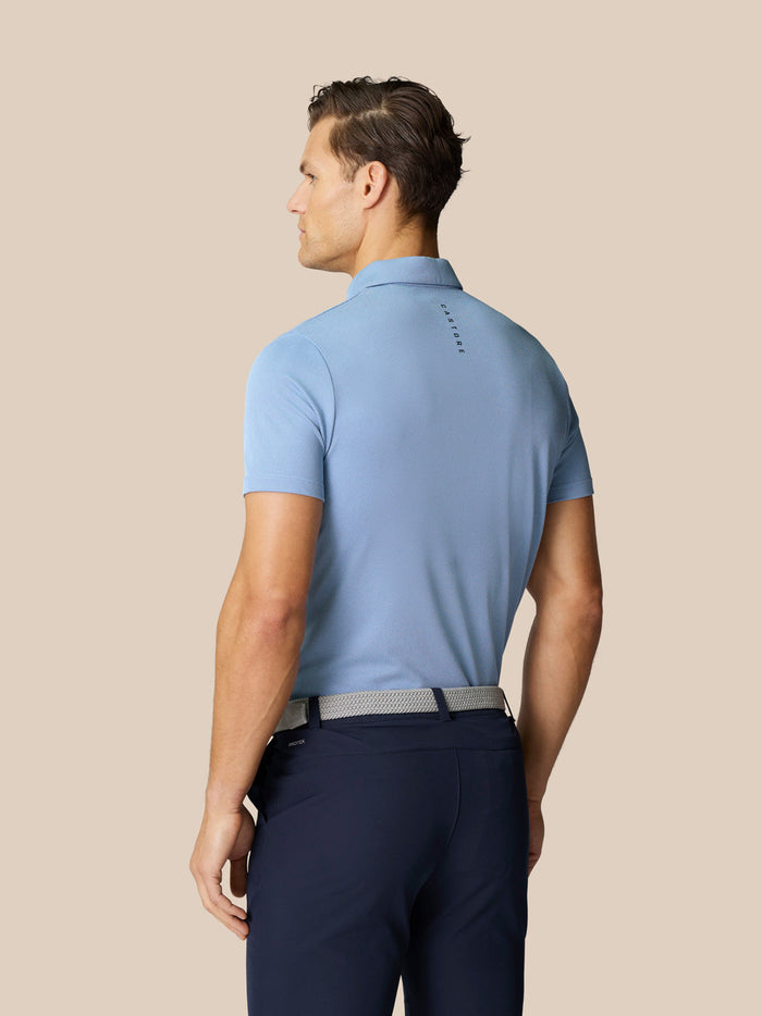 Back view of a male model in a sky blue polo tucked into navy pants with a belt, Castore branding on the back.