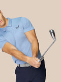 Male model in sky blue Castore Golf Pinnacle Polo mid golf swing with breathable knit fabric.