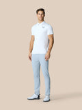 Full body shot of a man in a white polo and light blue pants standing with hands at his sides, Castore logo on the chest
