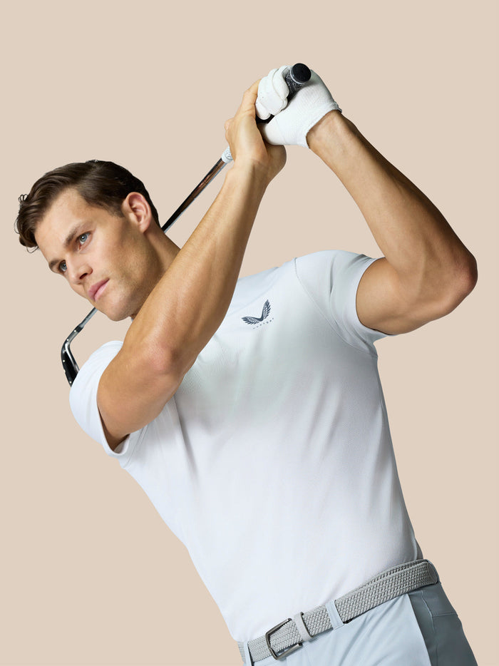 Male golfer in white Engineered Knit Polo mid swing with a raised golf club.