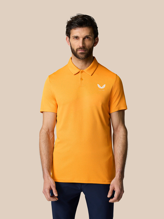 Male model in a bright mango Golf Pinnacle Polo with a pointed collar and Castore logo on the chest