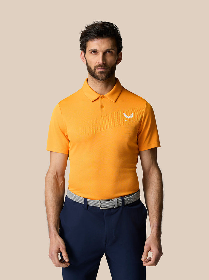 Male model wearing bright mango golf polo with collar and short sleeves; white logo on chest against a beige background.