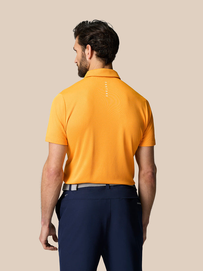 Back view of a man in a mango polo showing vertical Castore branding on the upper back.