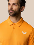 Close-up of bright orange polo showing textured knit and white Castore logo on the chest.