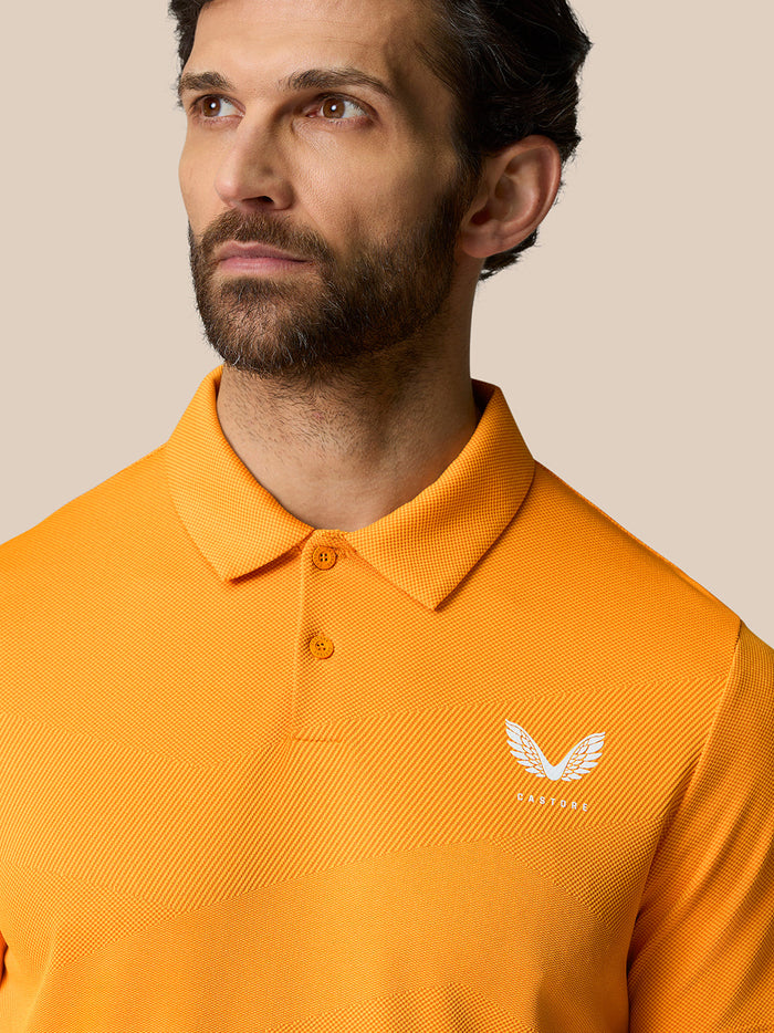 Close-up of bright orange polo showing textured knit and white Castore logo on the chest.