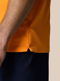 Close up of Golf Pinnacle Polo Mango orange textured knit fabric with a side hem vent.