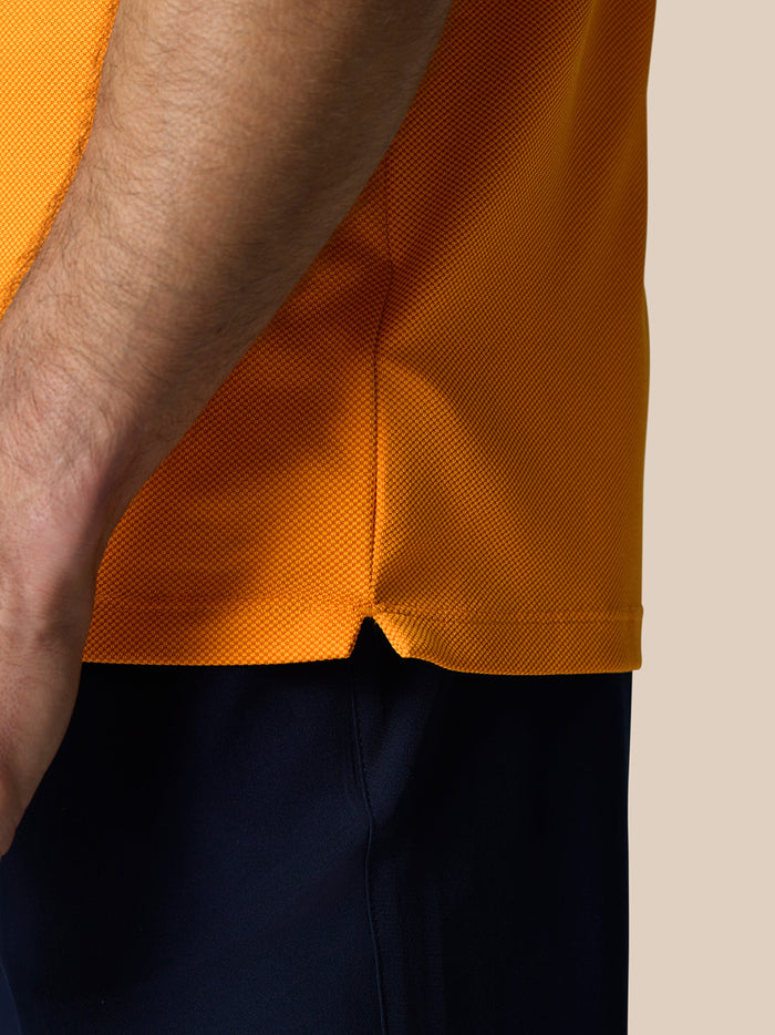 Close up of Golf Pinnacle Polo Mango orange textured knit fabric with a side hem vent.