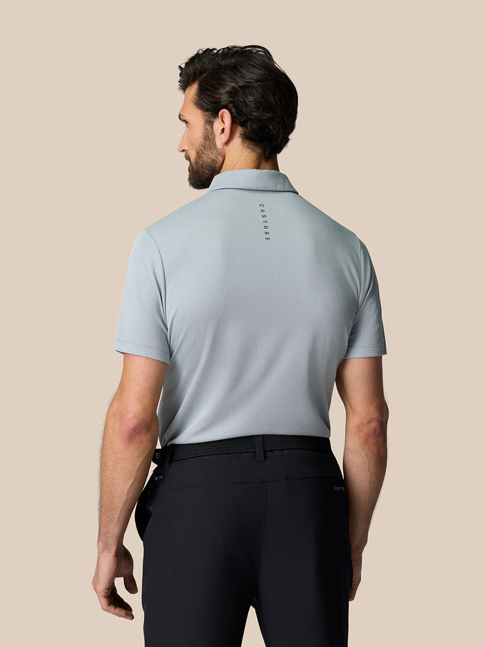 Back view of male model wearing a light grey Engineered Knit Polo with Castore branding along the upper back.