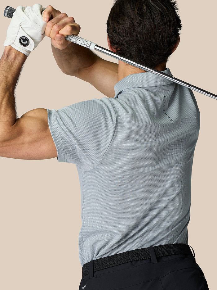 Golfer in a light blue polo seen from behind mid swing with a golf club raised.