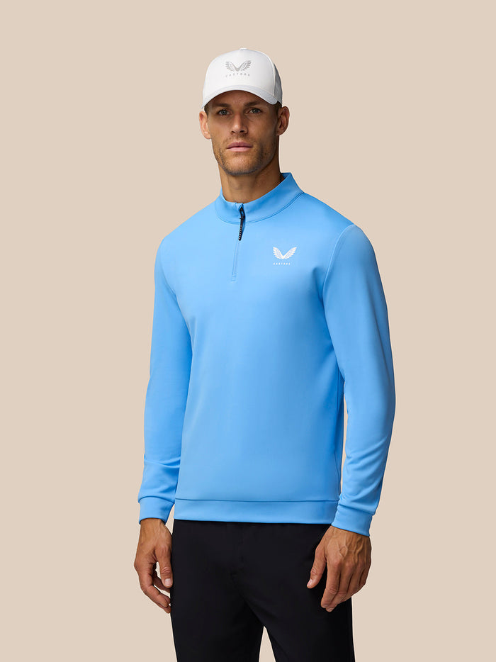 Male model wearing light blue Castore Golf Club Classic quarter zip top with funnel collar and left chest logo.
