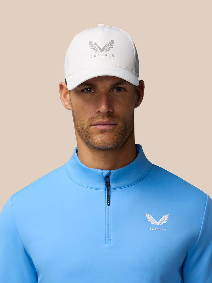 Golfer in white cap and blue quarter zip top with Castore logo on the chest.