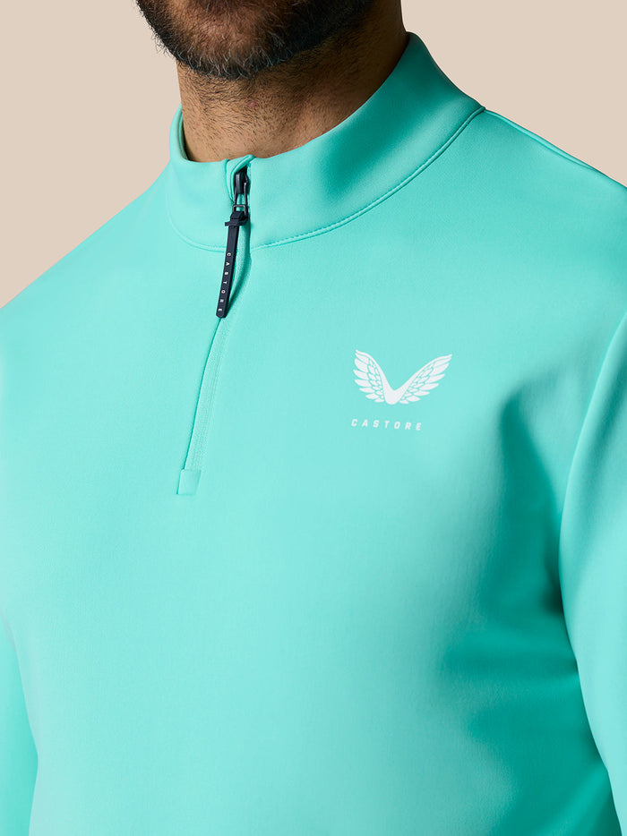 Close up of light aqua golf quarter zip top showing stand collar, zipper and Castore logo on chest.