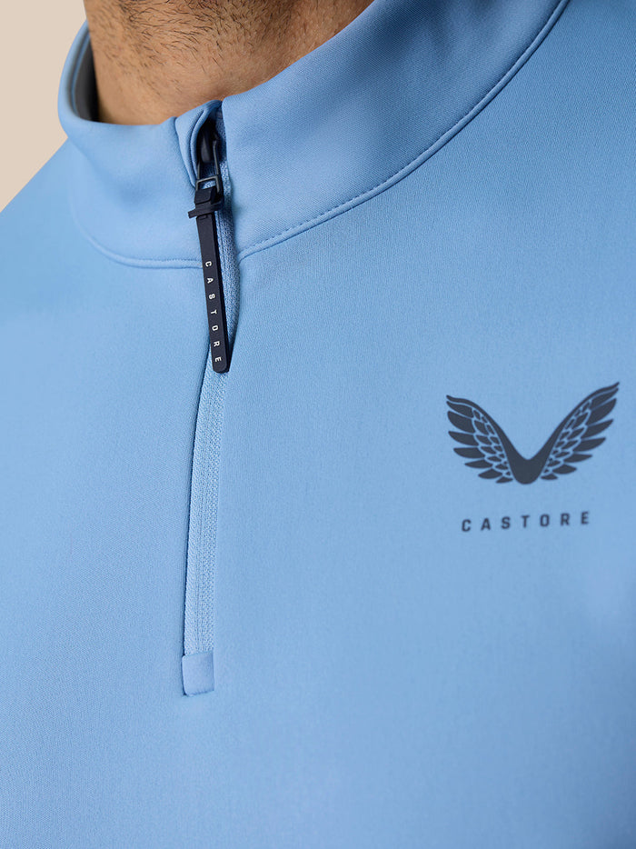 Close-up of the sky blue quarter zip top neckline showing zipper and Castore logo on chest.